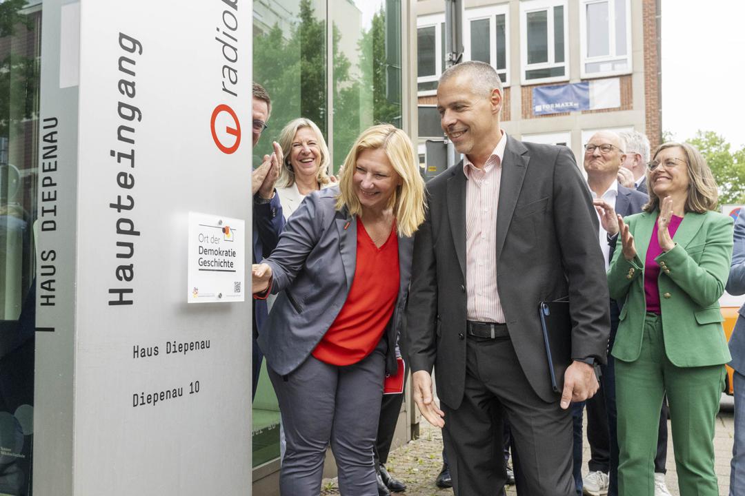 Radio-Bremen-Intendantin Yvette Gerner (links vorne) zeigt auf die Plakette, die Radio Bremen als Ort der Deutschen Demokratiegeschichte auszeichnet