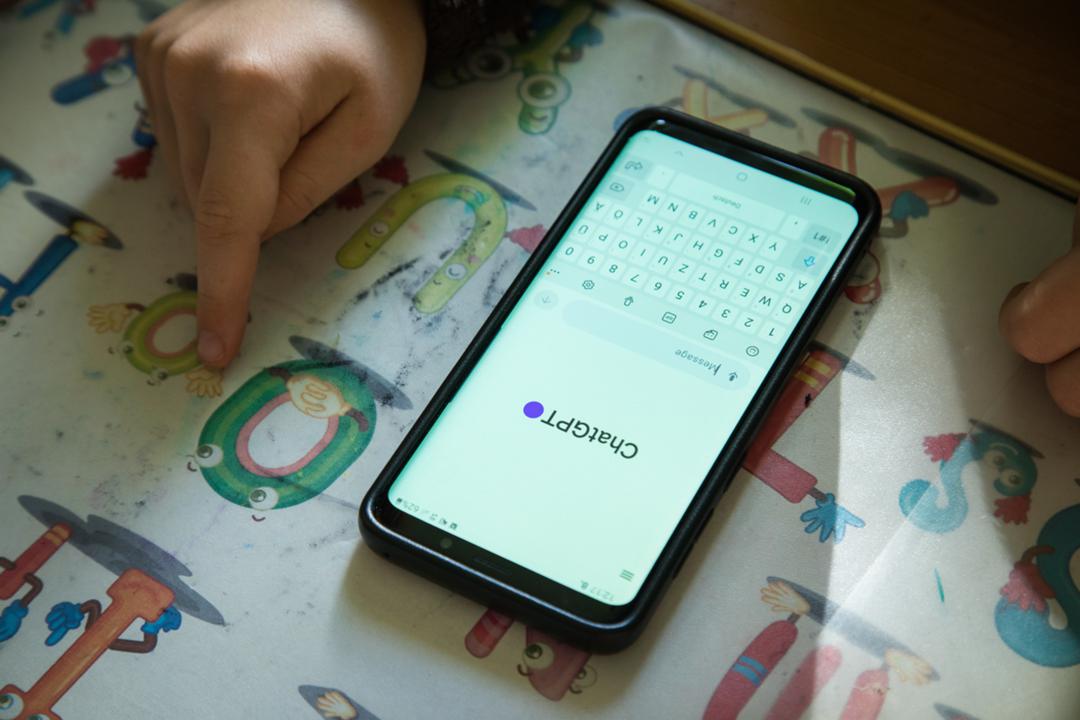 Ein Schüler sitzt an seinem Schreibtisch und hat die ChatGPT-App auf dem Smartphone geöffnet